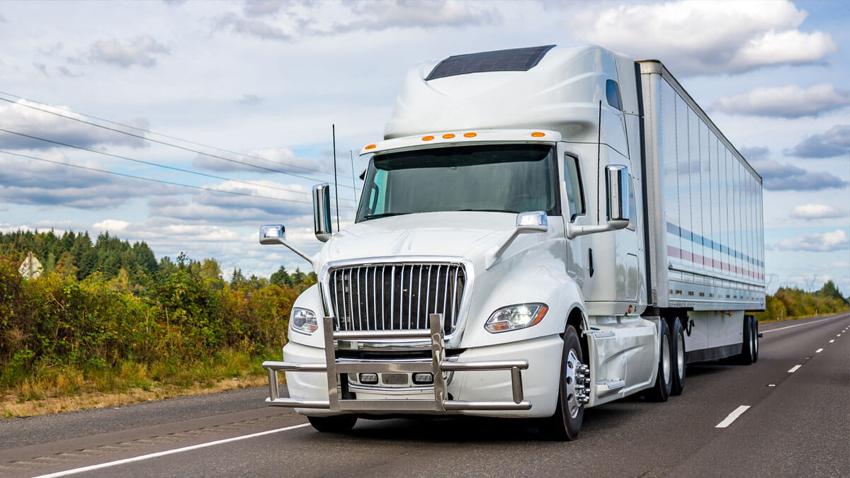 White semi truck pulling a dry van on a paved road.