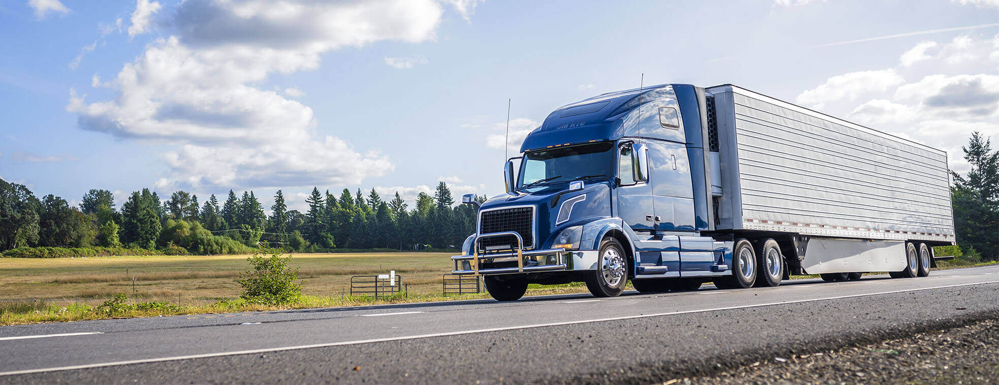 Blue semi pulling a reefer trailer down a road.