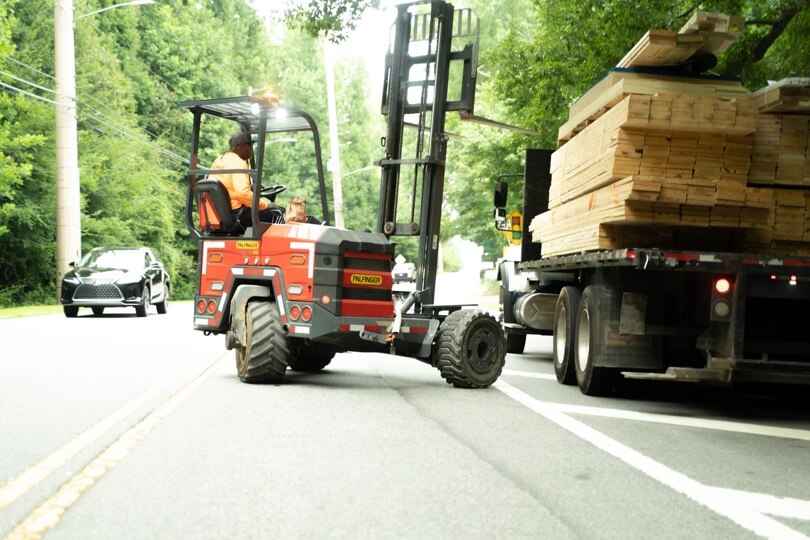 Palfinger Forklift unloading a truck loaded with wood planks.