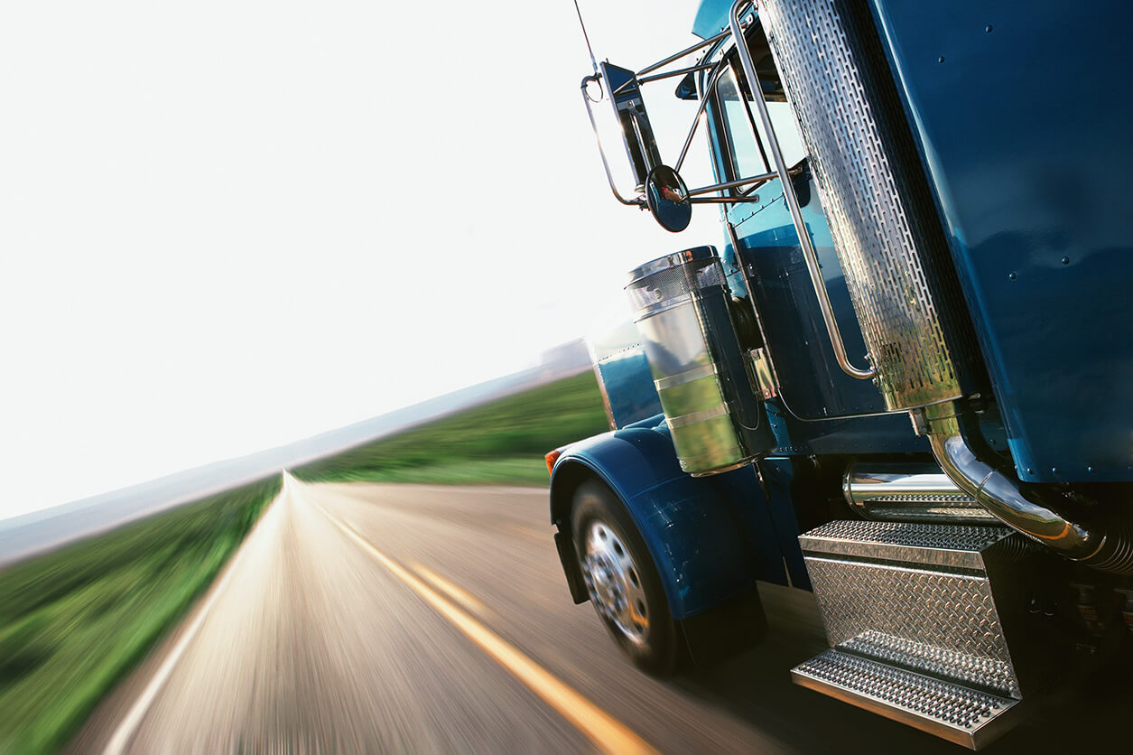 A blue semi truck traveling down an open stretch of highway.