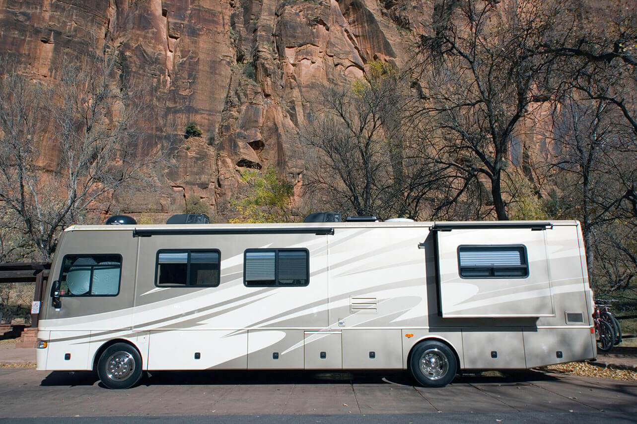 RV parked in front of a rocky mountain side.
